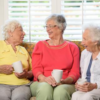 Three senior women enjoying a conversation while holding cups of tea.