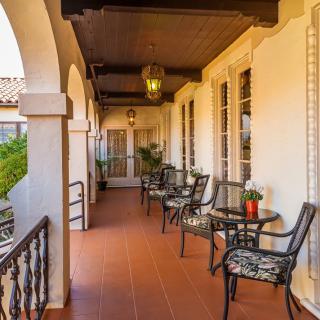 A charming veranda with arched architecture, featuring outdoor seating with tables and chairs, lit by a hanging lantern and decorated with potted plants.