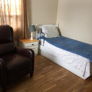 A cozy bedroom with a single bed, recliner chair, and nightstand.