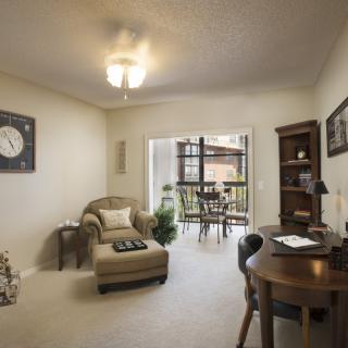 A cozy living space with a comfortable armchair, desk, and bookshelf, leading to an outdoor balcony.