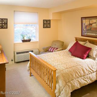 A cozy bedroom with a wooden bed frame, decorated with pillows and a quilted blanket, featuring a window allowing natural light.