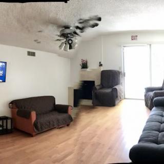 A spacious living room with a couch, armchair, fireplace, and a television mounted on the wall.