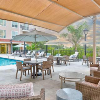 A luxurious poolside patio area with tables, chairs, and umbrellas under a large canopy.