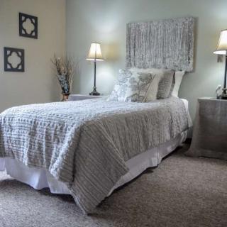 A cozy bedroom with a neatly made bed, decorated in neutral tones and enhanced by soft lighting from bedside lamps.
