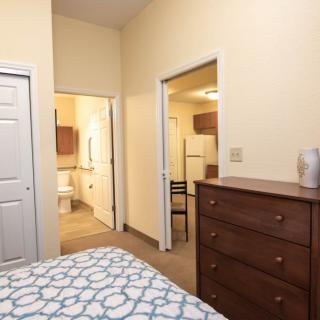 A cozy bedroom featuring a dresser, bed, and an open doorway leading to a bathroom.