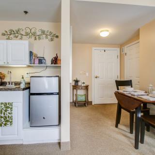 A cozy apartment interior featuring a small kitchen with white cabinets and a compact fridge, alongside a dining area with a neatly set table.