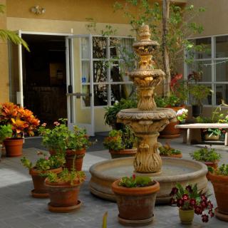 A tranquil courtyard featuring a multi-tiered fountain surrounded by various potted plants.