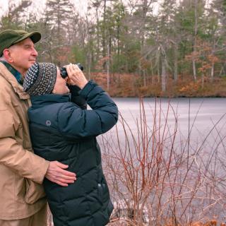 A couple birdwatching near a frozen lake in winter.