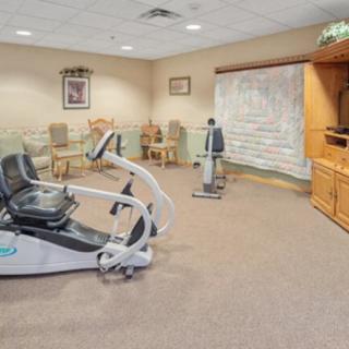 A small exercise room featuring a stationary bike and other fitness equipment, with chairs and a television for relaxation.