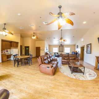 Spacious open-concept living area with leather sofas, ceiling fans, hardwood floors, and an adjacent kitchen.