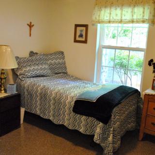 A cozy bedroom with a single bed, bedside table, lamp, and window letting in natural light.