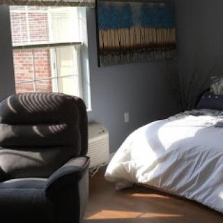 A cozy bedroom featuring a comfortable bed, a stylish armchair, and ample natural light streaming through the window.