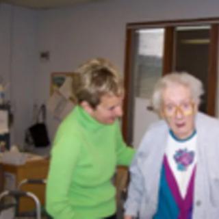 A caregiver assists an elderly woman in a nursing home setting.