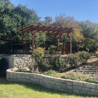 A scenic outdoor garden area featuring a pergola and landscaped stone walls.