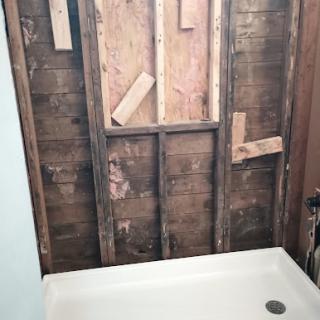An unfinished shower area showing exposed wood framing and a plastic shower base.