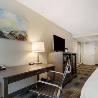 A cozy hotel room featuring a desk, lamp, and a television.