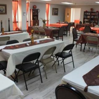 A community dining hall with tables and chairs neatly arranged, featuring tablecloths and decorative elements.