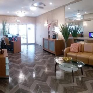 A modern office waiting room with a reception desk, sofa seating, and indoor plants.