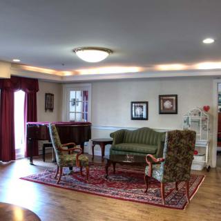 A cozy living room with classic furniture, including a sofa and chairs around a wooden table, adorned with a patterned carpet and a piano in the corner.