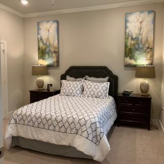 A well-decorated bedroom with a neatly made bed, bedside tables, lamps, and wall art.