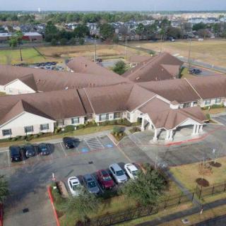 Aerial view of a large building with a parking lot and surrounding landscaping in a suburban area.