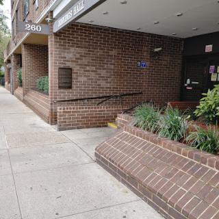 A view of a brick building entrance with landscaped greenery along the sidewalk.