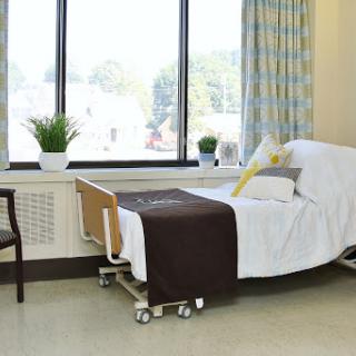 A peaceful hospital patient room featuring a neatly made bed and natural light coming through the window.