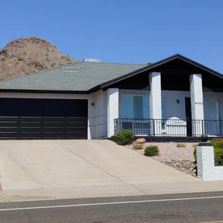 A modern single-story house with a garage and driveway set against a mountainous backdrop.