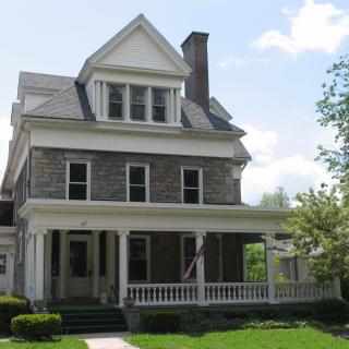 A large two-story colonial-style house with a front porch and gabled roof.