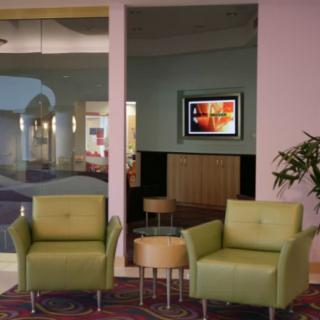 A modern lobby area with green armchairs and a small table, featuring stylish decor.