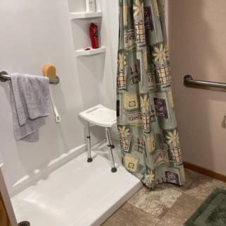 A bathroom featuring a shower with a chair, grab bar, and patterned shower curtain.