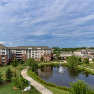A scenic view of a residential complex with a pond and fountain surrounded by greenery.