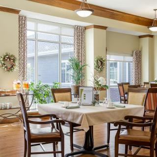 A well-lit dining area with neatly arranged tables and chairs, featuring large windows and tasteful decorations.