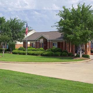 A suburban brick house with a well-maintained lawn and trees, featuring an American flag and a driveway.