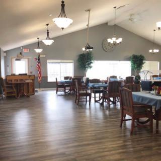 A spacious dining area with tables and chairs, featuring wooden flooring and ceiling lights.