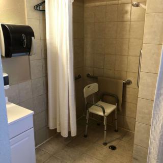An accessible bathroom featuring a shower with a curtain, grab bars, and a shower chair.