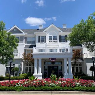 A charming hotel building with well-maintained landscaping, featuring vibrant flowers and lush trees under a clear sky.