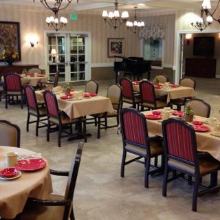 An elegantly decorated dining room with neatly arranged tables and chairs, featuring chandeliers and a grand piano in the background.