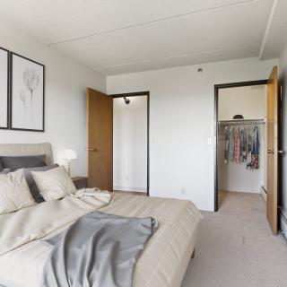 A modern, minimalist bedroom with a neatly made bed and an open closet.