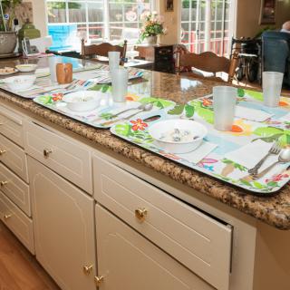 A kitchen counter with table settings prepared on colorful placemats.