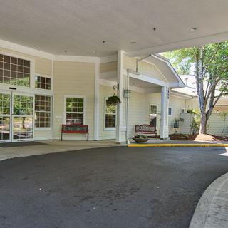 The image shows the entrance of a building with a covered driveway, benches, and large windows.