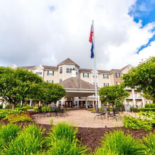 A beautiful building with a well-maintained garden and flags flying in front, set against a partly cloudy sky.