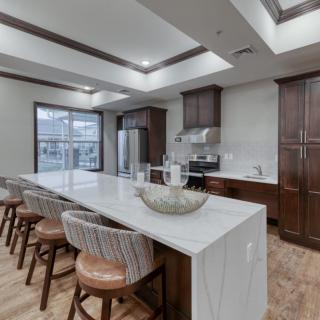 A modern kitchen featuring a large island counter with bar stools, wood cabinets, and stainless steel appliances.