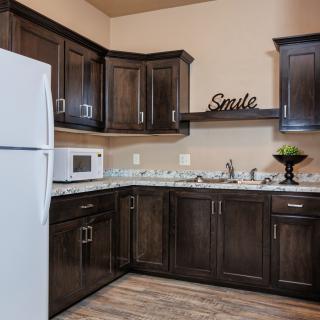 A modern kitchen with dark wood cabinets, a white refrigerator, and a microwave.