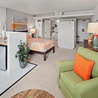 A modern apartment interior featuring a cozy living area with bright green and orange accents, adjacent to an open bedroom space.