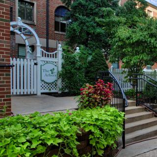 A charming entrance gate surrounded by lush greenery and a brick building.