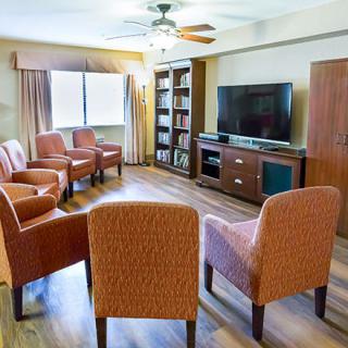 A cozy living room with multiple chairs arranged around a television set, complete with a ceiling fan and bookshelf.
