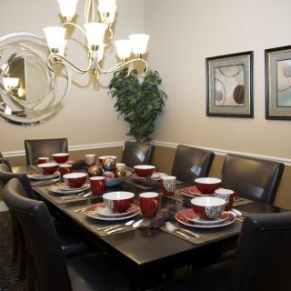 A well-decorated dining room with a formal table setting, featuring red dishware and an elegant chandelier.