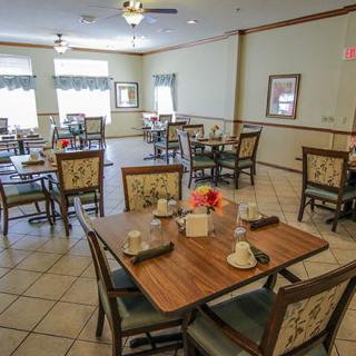 An empty dining area with neatly arranged tables and chairs, featuring natural lighting through large windows.