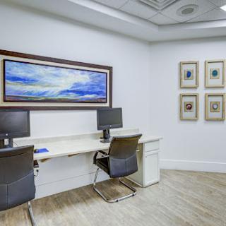 A modern office space featuring a desk with computers, stylish chairs, and framed artwork on the walls.